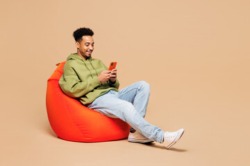 Full body young man of African American ethnicity wearing green hoodie casual clothes sit in bag...