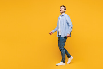 Fototapeta premium Full body side profile view young smiling cheerful fun happy man he wear blue shirt t-shirt casual clothes walking going isolated on plain yellow orange background studio portrait. Lifestyle concept.