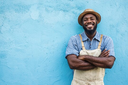 Smiling man in a straw hat and apron stands confidently against a vibrant blue wall, showcasing joy
