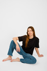 Young woman poses casually in black shirt and jeans against a white background