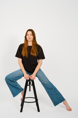 Young woman striking a confident pose on a stool against a plain background