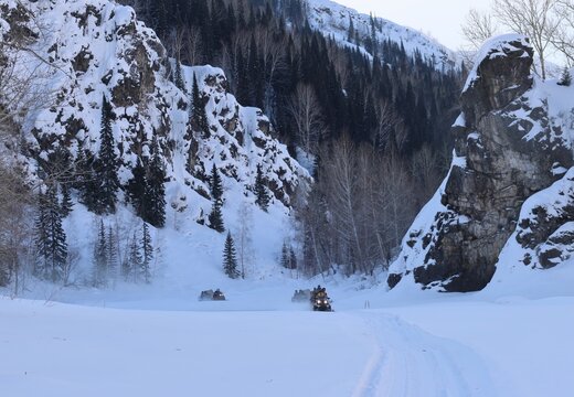 a group of tourists on snowmobiles on the frozen Malaya Ulba River in the mountains of Eastern Kazakhstan in winter