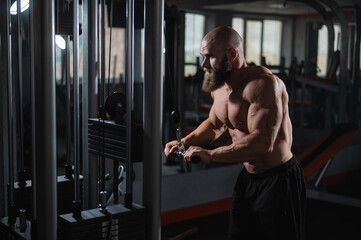 Naklejka premium Bald Caucasian Bodybuilder doing heavy triceps exercises with cable. 