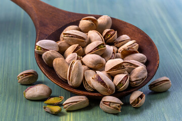 Freshly shelled pistachios in a wooden spoon resting on a colorful surface