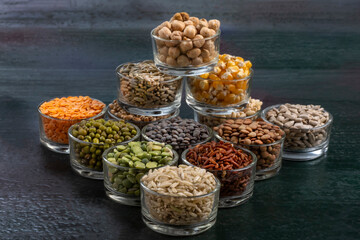 Variety of dried legumes and seeds arranged neatly in glass containers on a dark wooden surface