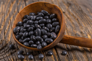 Black beans in a wooden spoon resting on a rustic wooden surface highlighting their smooth texture and rich color