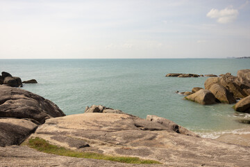 A landscape of beautiful rocks around the ocean. Sunlight reflects off the water, creating a shimmering effect. The scene conveys a sense of calmness: soft waves rolling over the rocks.