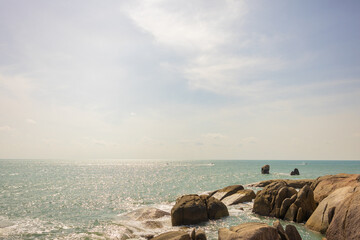 A landscape of beautiful rocks around the ocean. Sunlight reflects off the water, creating a shimmering effect. The scene conveys a sense of calmness: soft waves rolling over the rocks.