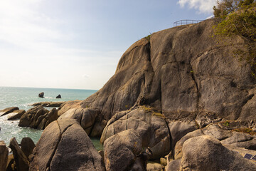 A landscape of beautiful rocks around the ocean. Sunlight reflects off the water, creating a shimmering effect. The scene conveys a sense of calmness: soft waves rolling over the rocks.