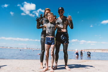 A family relaxes by a salt lake. Their bodies are covered in black healing mud.