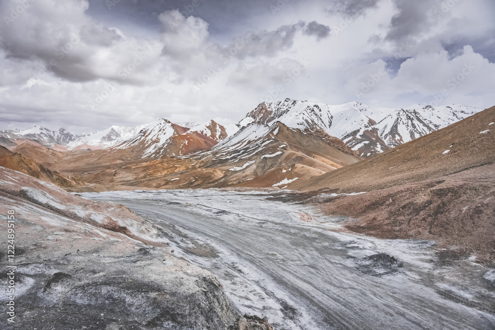 Wall mural Dusty high-mountain road of Pamir Highway and Ak-Baital Pass, panoramic landscape in rocky mountains with snow in Tien Shan Mountains in Tajikistan