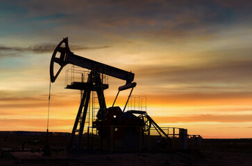 Crude oil pump jack at oilfield on atmospheric sunset backround. Fossil crude output and fuels oil...