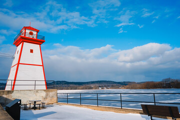 Fototapeta premium Painted in red and white lighthouse by the river, winter, Grenville, Canada