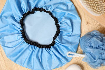 Shower cap and bath accessories on wooden background, flat lay