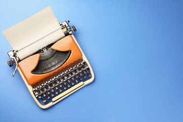 Vintage typewriter with sheet of paper on blue background, top view. Space for text