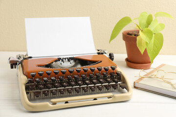 Vintage typewriter with sheet of paper, glasses, notebook and houseplant on white wooden table