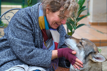 Smiling mature woman gently petting czechoslovakian wolfdog in garden
