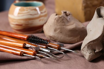 Set of different crafting tools and pieces of clay on table, closeup
