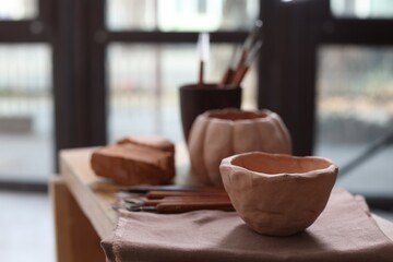 Handmade ceramic bowl and set of different crafting tools on shelf indoors