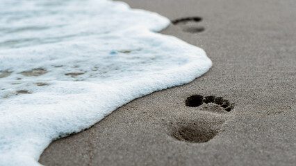 footprints in the sand on the beach near the surf