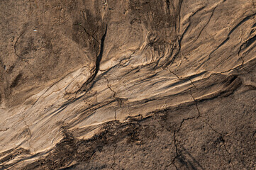 Cracked, dry earth with layered sedimentary rock formations, displaying erosion patterns and geological textures