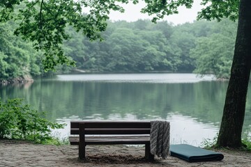 Obraz premium Serene lakeside bench with a cozy blanket and yoga mat amidst lush greenery and tranquil water