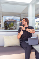 Obraz premium A happy hipster man gives thumbs up, points to the left while working in the office, vertical photo