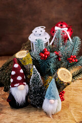 two cute white-bearded gnomes against the background of a Christmas tree, branches, holly berries and Christmas decor, New Year celebration concept