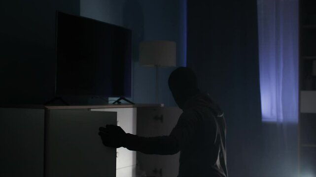 trespassing, dangerous man in balaclava rummages through chest of drawers in search of money and jewelry at night