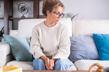 A woman sitting alone on the couch at home, looking down with a sad expression, feeling emotionally drained and reflecting on relationship issues and personal struggles during menopause, burnout