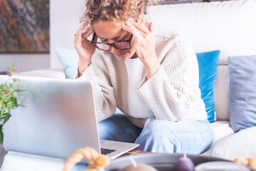 A woman working in her home office, dressed casually, looking frustrated but focused, using her laptop to solve work problems, navigate websites, and engage in online tasks for her digital business
