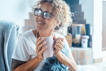 An adult woman enjoying her personal time at home, holding a cup of hot tea or coffee, appearing...