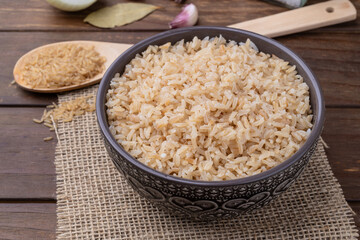 Cooked brown whole rice in a bowl over wooden table with onion, bay leaf and garlic