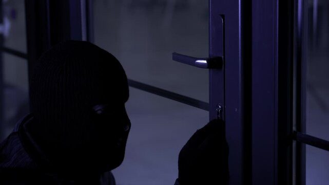 dangerous man in balaclava in gloves with picklocks tries to pick the lock and open door to room at night