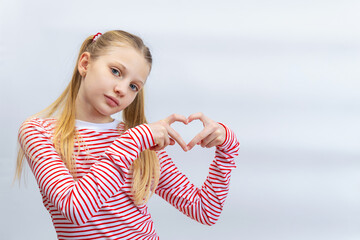 Girl forming a heart shape with her hands in a striped shirt. Space for text.