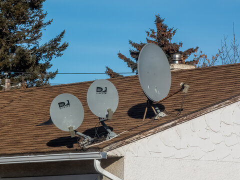 Calgary, Alberta, Canada. Jan 27, 2025. Three satellite dishes, pointing towards the sky, are mounted on a residential rooftop, providing access to a world of entertainment.