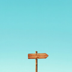 Fototapeta premium Wooden arrow sign on a pole with a clear blue sky in the background, symbolizing direction or guidance, representing travel, navigation, and decision-making.