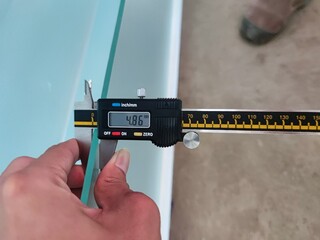 Digital caliper measuring the thickness of a glass panel to ensure accuracy in construction and...