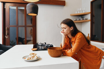 A thoughtful woman in an orange outfit contemplating over a bowl in a modern kitchen, reflecting on healthy eating and lifestyle choices © SHOTPRIME STUDIO