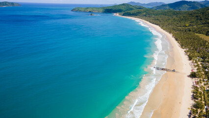 An expansive aerial view showcases a vast turquoise coastline merging with lush greenery, epitomizing a tropical paradise and inviting exploration and admiration.