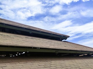 View of a worn asphalt shingle roof under a bright blue sky, showing visible damage and signs of aging on the roofing structure