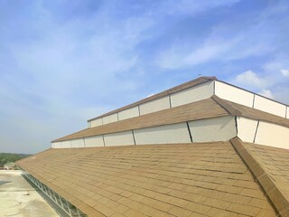 Obraz premium Damaged shingle roof with visible gaps and wear, highlighting structural vulnerability under a bright and partly cloudy sky