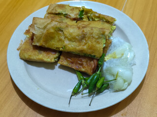 Egg martabak. Egg martabak is a traditional Indonesian food that tastes savory and delicious, served on a plate with pickles and chili.