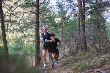 Obraz premium Man and woman running uphill on a forest trail during a workout.