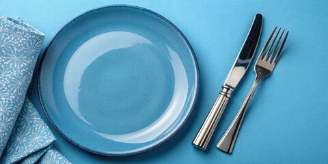 empty blue plate with knife and fork on blue background, everyday objects, simple composition, blue hue, culinary accessories