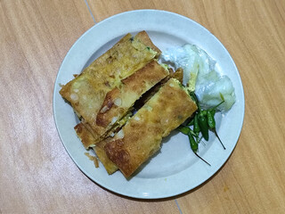 Egg martabak. Egg martabak is a traditional Indonesian food that tastes savory and delicious, served on a plate with pickles and chili.