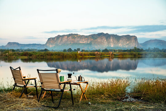 Morning happiness with a coffee drip set, camping chair, beautiful natural view of Phu Pha Man reflecting on water in Khon Kaen Province, Thailand. Travel and camping lifestyle on holiday.