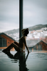 Woman relaxes by the poolside amid a tranquil backdrop of mountains and overcast skies