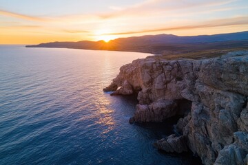 A dramatic sunset casts golden hues on rugged coastal cliffs, reflecting the beauty of nature and the enchanting colors of twilight over the tranquil ocean.