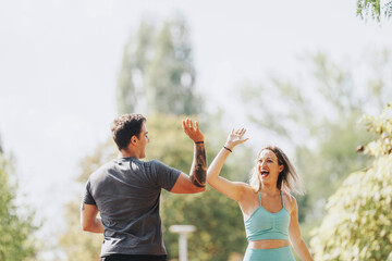 Naklejka premium Two friends enjoy exercising together in a sunny park, sharing a high-five filled with enthusiasm and positivity. The image captures the joy of fitness and friendship outdoors.